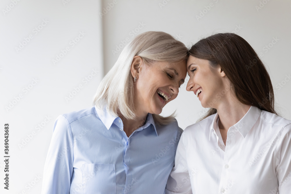 Cheerful mature mother touch foreheads embrace adult daughter laughing enjoy meeting, having fun feels overjoyed remember life moments. Comfort and understanding between two diverse generation concept Cheerful mature mother touch foreheads embrace adult daughter laughing enjoy meeting, having fun feels overjoyed remember life moments. Comfort and understanding between two diverse generation concept