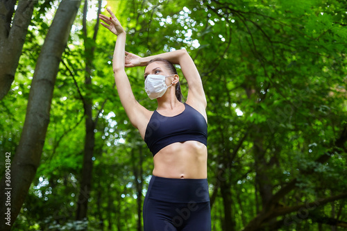 A ballerina in a mask and pointe shoes is doing exercises on a wooden path in a forest park. safe outdoor training concept