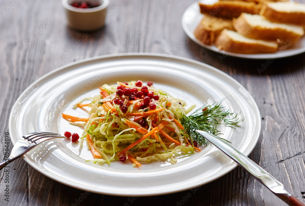 Fresh cabbage salad made from shredded white cabbage, carrots and berries on a white plate. Top view, wooden background, selective focus