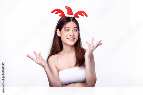 Portrait of beautiful charming young Asian woman wearing red reindeer horns and Santa hat costume on white background, portrait Christmas holiday advertising concept.