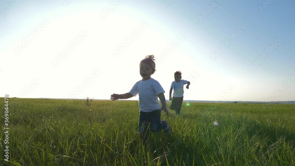 Two children in white t-shirts running on green fresh grass. Happy children enjoy life. The concept of teamwork. Two children in white t-shirts running on green fresh grass. Happy children enjoy life. The concept of teamwork.