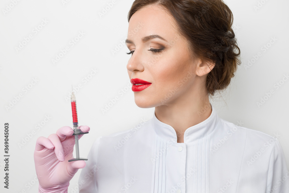 Portrait of a female doctor beautician holding a syringe with an injection in her hand. Lip augmentation. Skin care in a beauty salon. Portrait of a female doctor beautician holding a syringe with an injection in her hand. Lip augmentation. Skin care in a beauty salon.