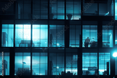 a window with a view through horizontal blinder. business people working inside. businee office building. night scene photo