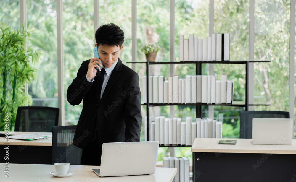 Young Asian businessman talking on the phone while working with laptop computer in the office. Young Asian businessman talking on the phone while working with laptop computer in the office.