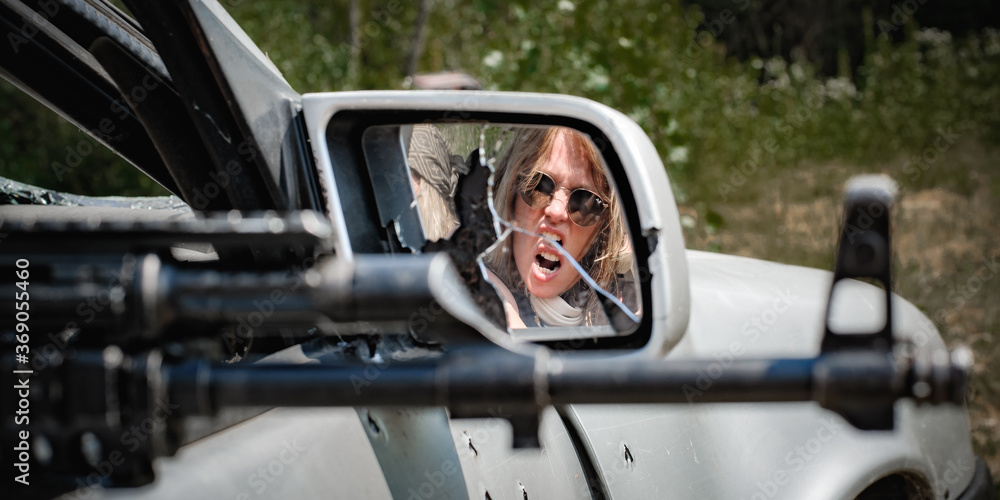 Abstract view in mirror of aggressive female soldier shooting from car with rifle machine gun. Woman with weapon. Femme fatale