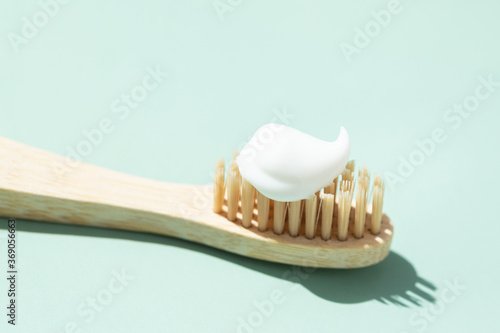 Bamboo toothbrush with toothpaste on mint background. Close up view in sunlight.