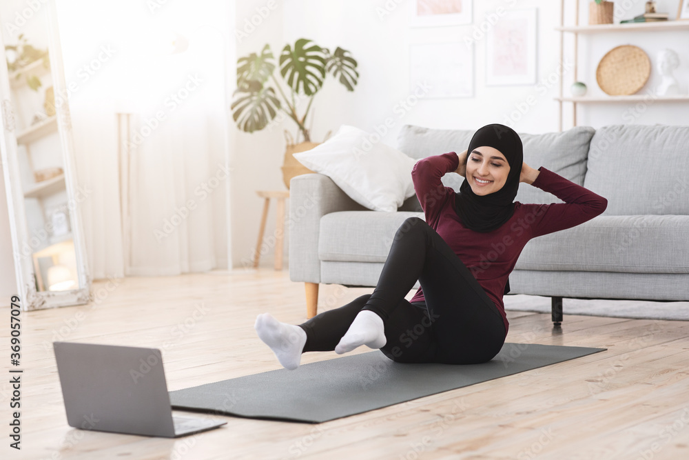 Sporty arabic woman in hijab doing abs exercises with laptop at home Sporty arabic woman in hijab doing abs exercises with laptop at home