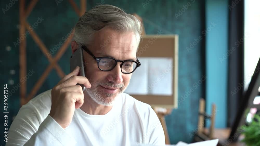 Mature businessman at his desk talking on smartphone Mature businessman at his desk talking on smartphone