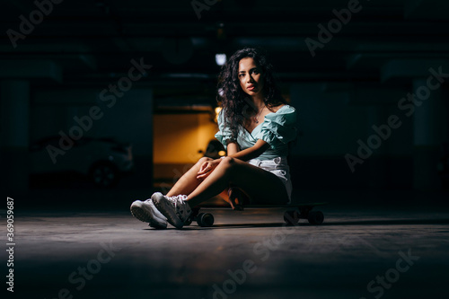 Beautiful afro american girl sitting on a skateboard in the underground Parking