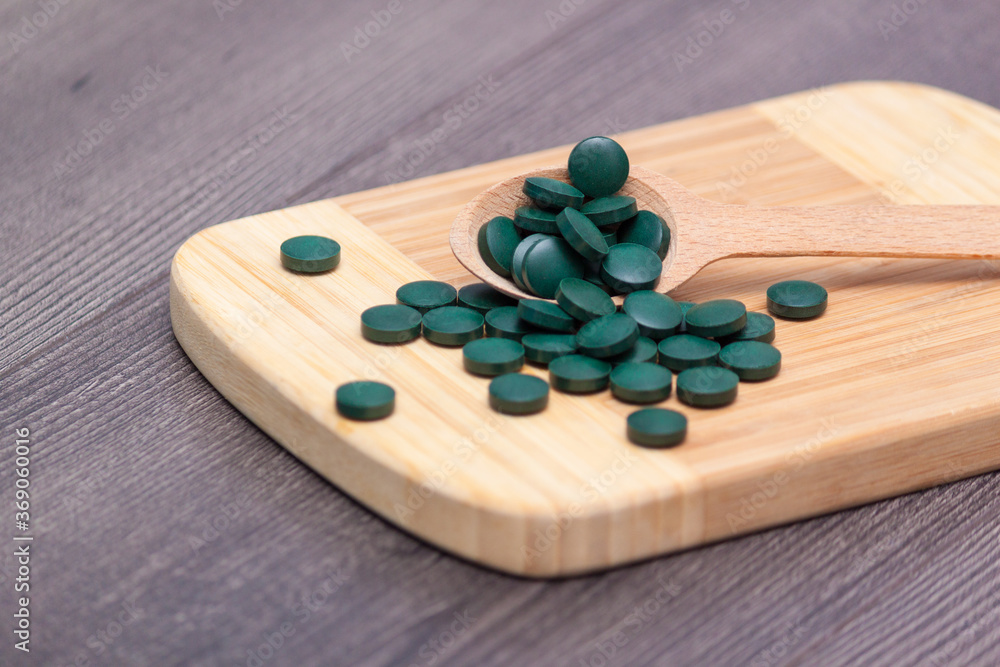 Green tablets - spirulina or chlorella in a wooden spoon. Healthy living concept. Green tablets - spirulina or chlorella in a wooden spoon. Healthy living concept.