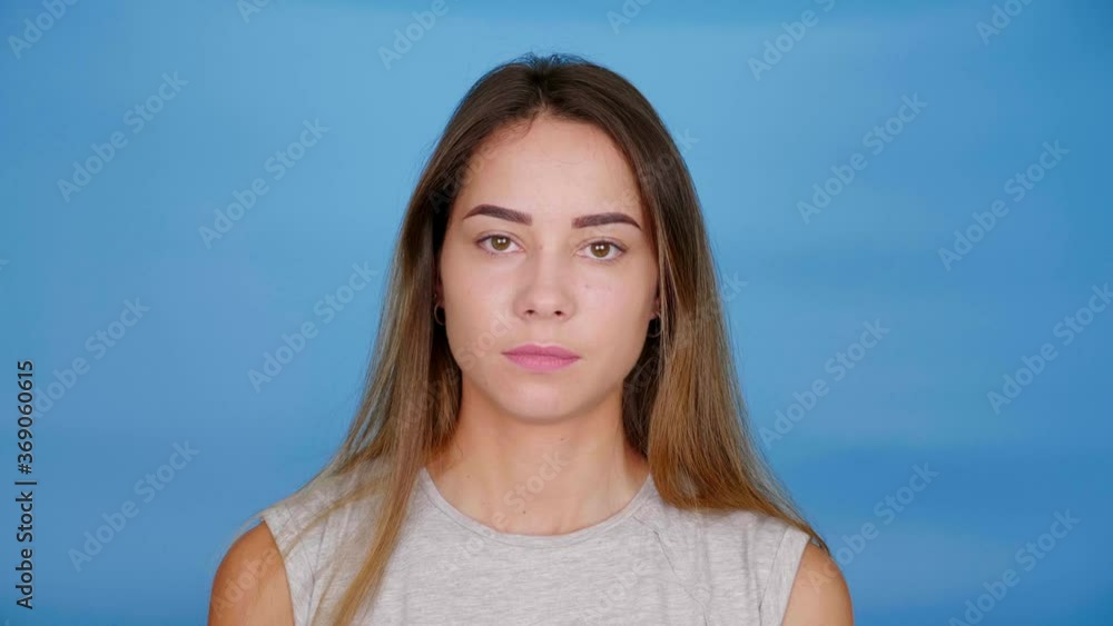 Woman in gray t-shirt looks camera on blue background with copy space. 4K slow motion footage Woman in gray t-shirt looks camera on blue background with copy space. 4K slow motion footage