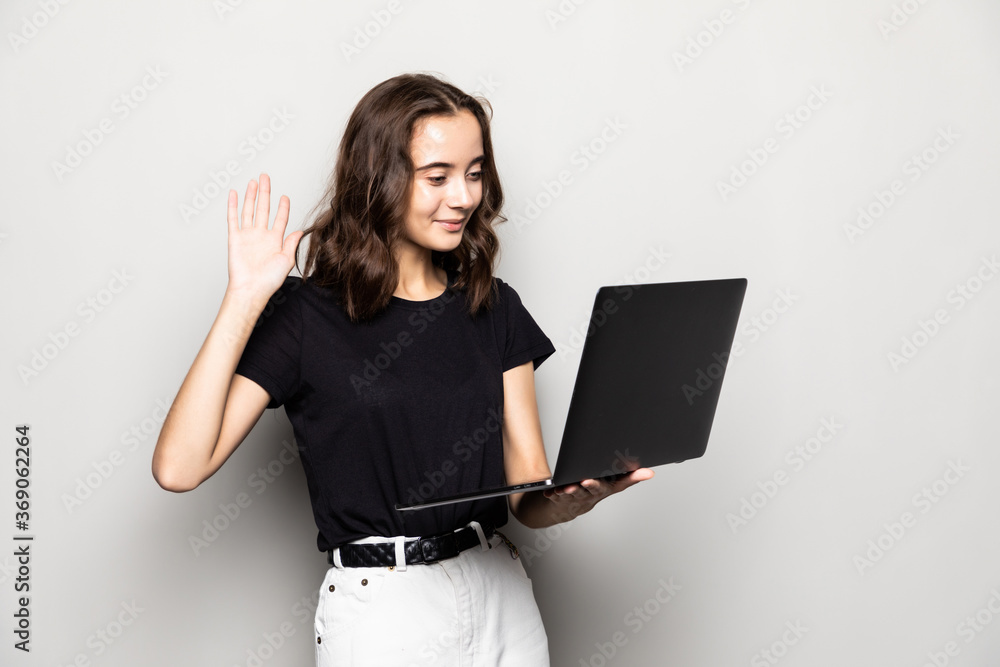Portrait of a happy pretty girl holding laptop and waving while having video conversation over gray background Portrait of a happy pretty girl holding laptop and waving while having video conversation over gray background