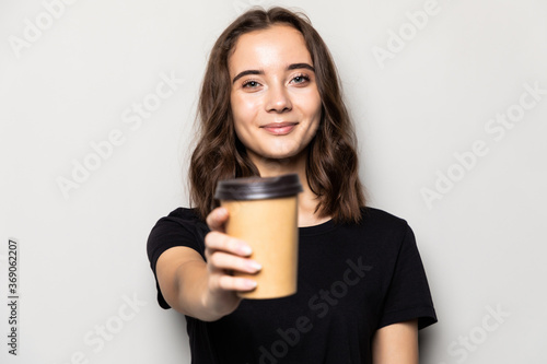 Young beautiful woman offers cup of coffee isolated on gray background