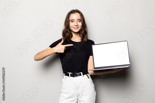Portrait of a smiling woman pointing finger on blank laptop screen over gray background