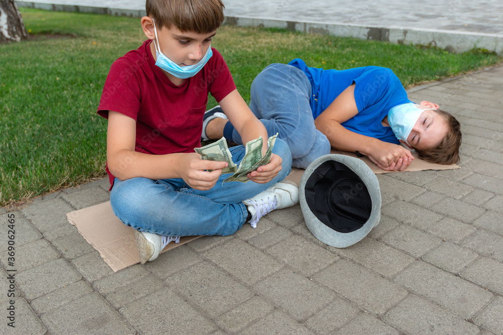 Naklejka premium The boy counts the money begged from passers-by on the street. His brother is sleeping next to him on a piece of cardboard.