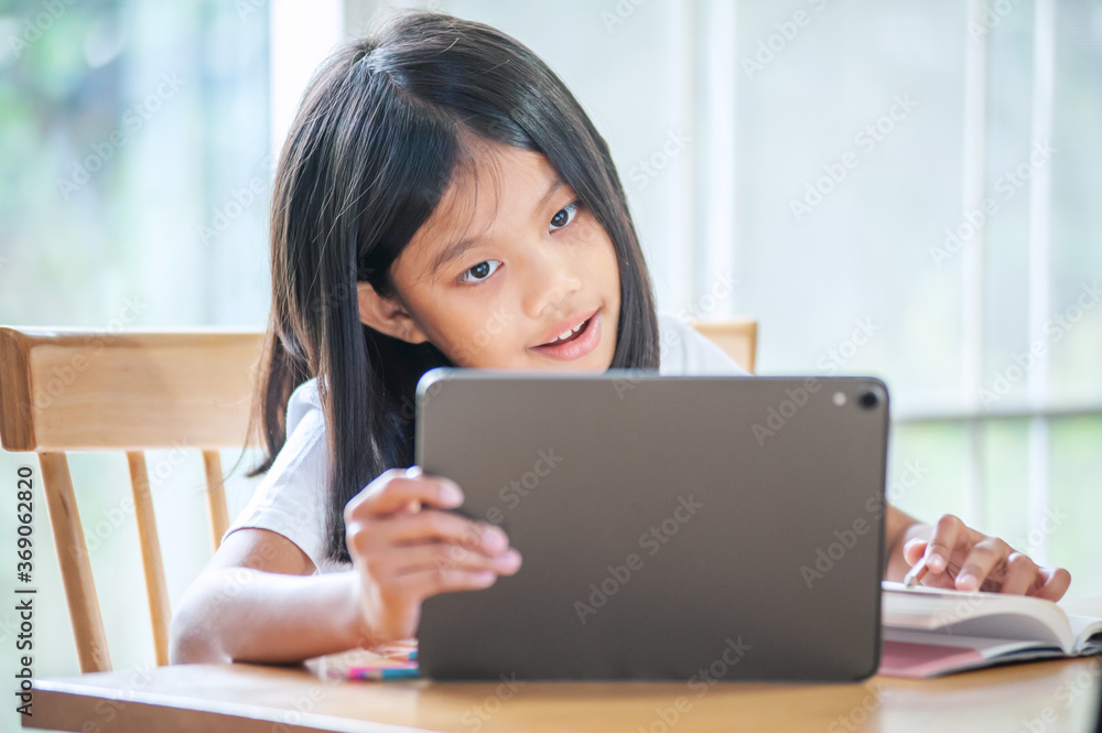 little asian girl studying online at home and using tablet for Homeschool Quarantine coranavirus pandemic New normal concept little asian girl studying online at home and using tablet for Homeschool Quarantine coranavirus pandemic New normal concept