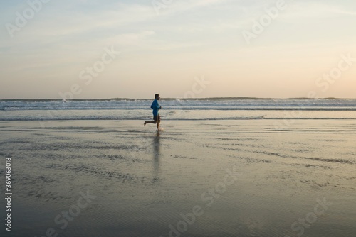 outdoors running workout - young attractive and athletic runner man jogging on beautiful beach in Summer training happy and free in fitness and healthy lifestyle concept