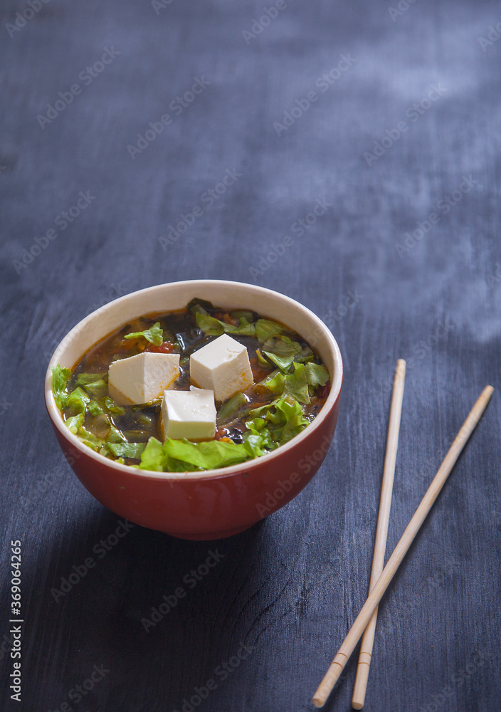 Japanese soup with tofu cheese and vegetables, chopsticks on black background. Copy spaes.