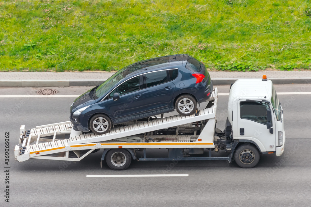 Passenger car loaded onto an evacuation truck rides along the road, aerial side view.