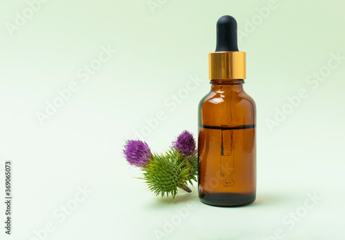 Mock up glass cosmetic brown bottle with a pipette on a mint background. There is a burdock near the jar. Health topic.
