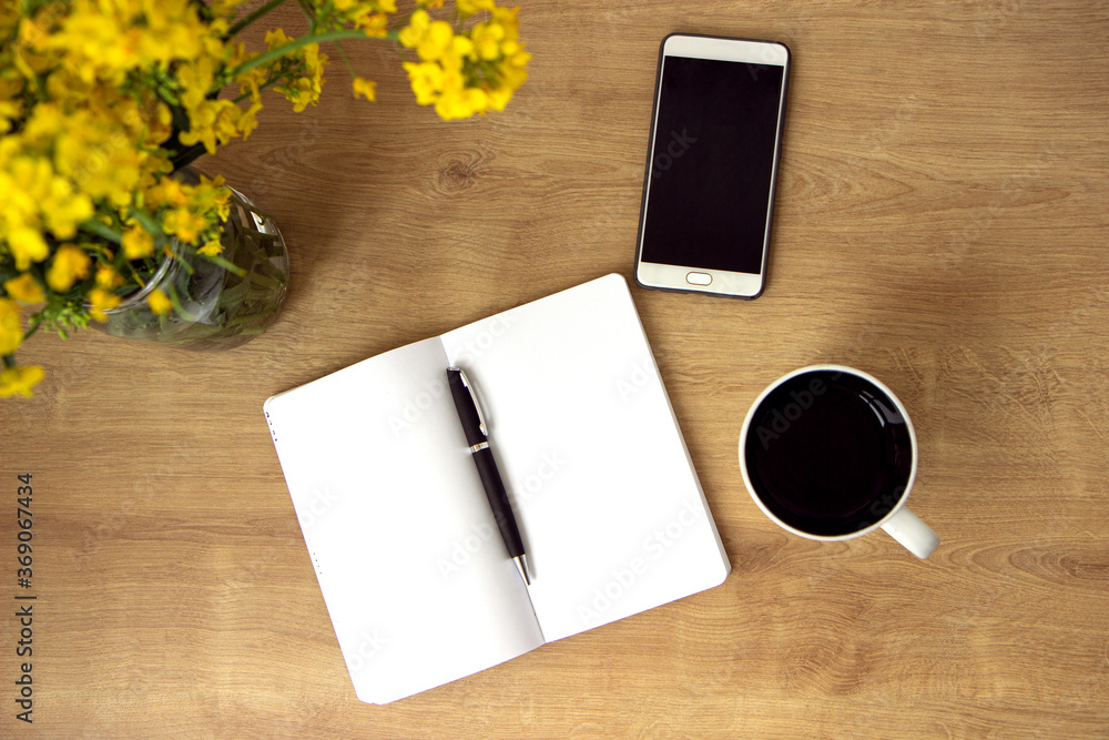 Open notebook with clean leaves with cup of tea, smartphone and vase with yellow flowers rapeseed on table Open notebook with clean leaves with cup of tea, smartphone and vase with yellow flowers rapeseed on table
