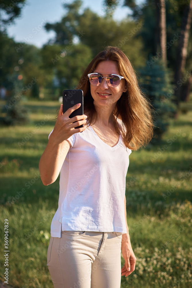 Girl blogger writes a post in the park. Young girl walking in the park with a phone in her hands. ?ommunication via phone. chatting in the park