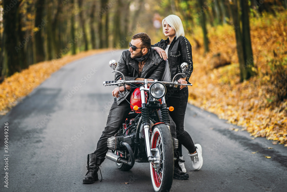 Pretty couple near red motorcycle on the road in the forest with colorful blured background Pretty couple near red motorcycle on the road in the forest with colorful blured background