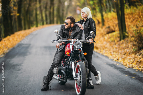 Pretty couple near red motorcycle on the road in the forest with colorful blured background © bedya