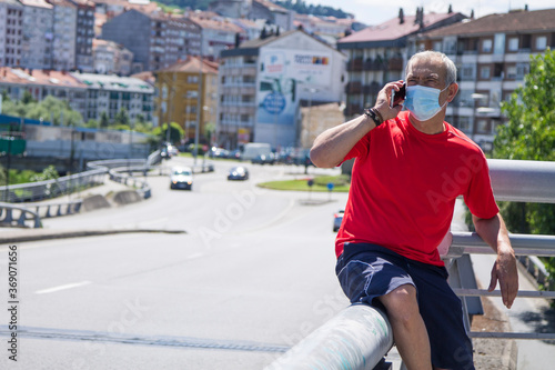 mature man with medical mask doing sports and using mobile phone in the city, concept of sport and technology in the new normal