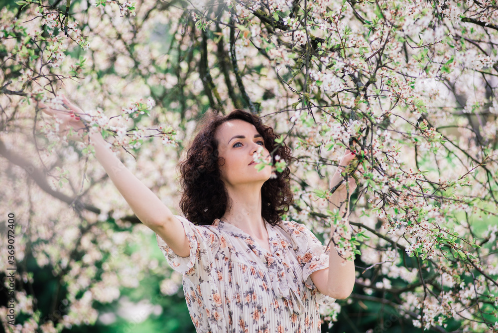 Young attractive woman with curly long hair posing in spring blooming garden, apple trees Young attractive woman with curly long hair posing in spring blooming garden, apple trees