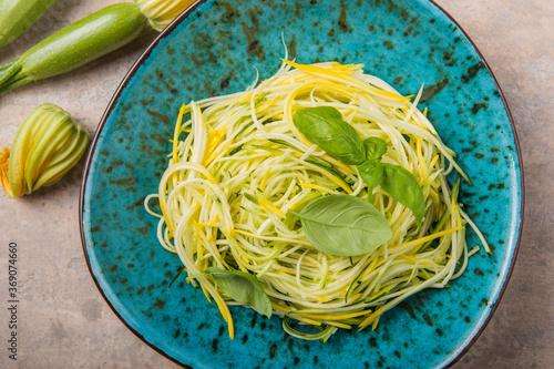 Zucchini vegetable noodles - green zoodles or courgette spaghetti on plate over gray background. Clean eating, raw vegetarian food concept. Copy space for text. Top view or flat lay