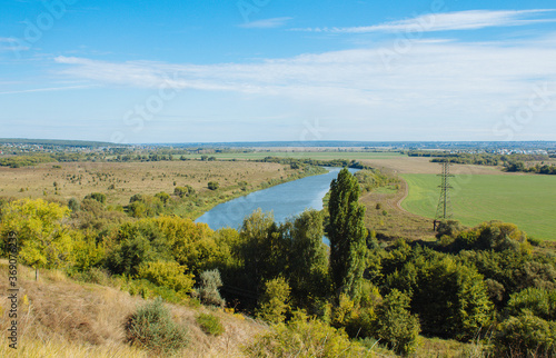 Blue sky, green grass.  A wide river flows in the middle of the field, a beautiful nature view from the top. © Vera