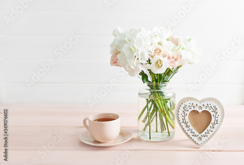 Bouquet of roses  eustomas and hydrangeas on table. Cup of tea and photo frame. Greeting card for mothers day. Cozy good morning. Happy Birthday. Romantic breakfast. Flowers composition for Valentine