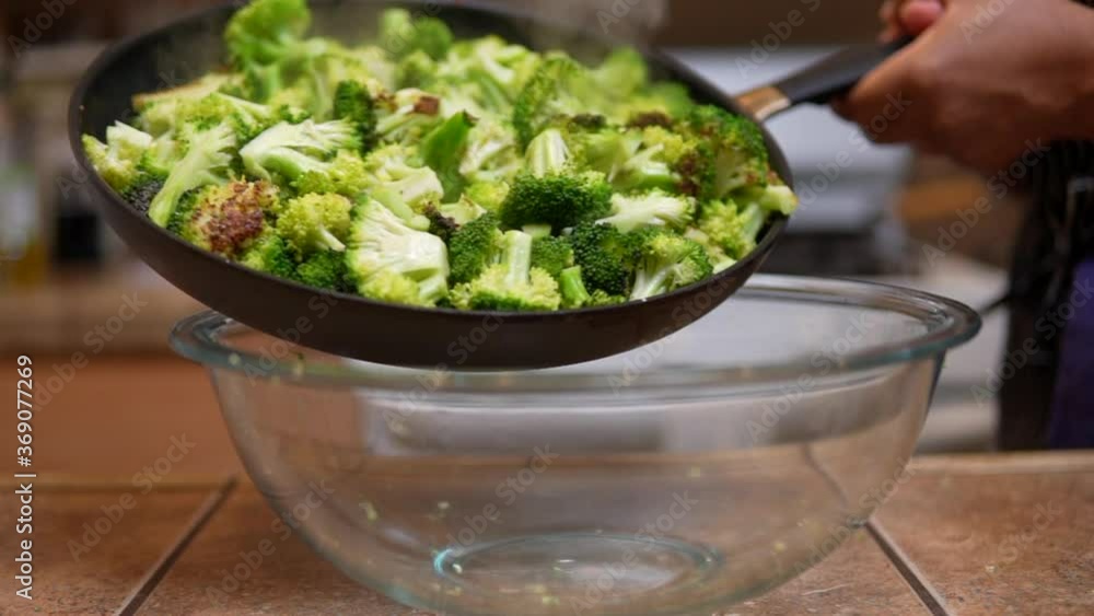 Carefully shaking a pan full of freshly cooked broccoli into a glass bowl - slow motion Carefully shaking a pan full of freshly cooked broccoli into a glass bowl - slow motion