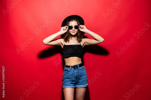 Young pretty woman wearing sunglasses and floppy hat isolated on red background © dianagrytsku