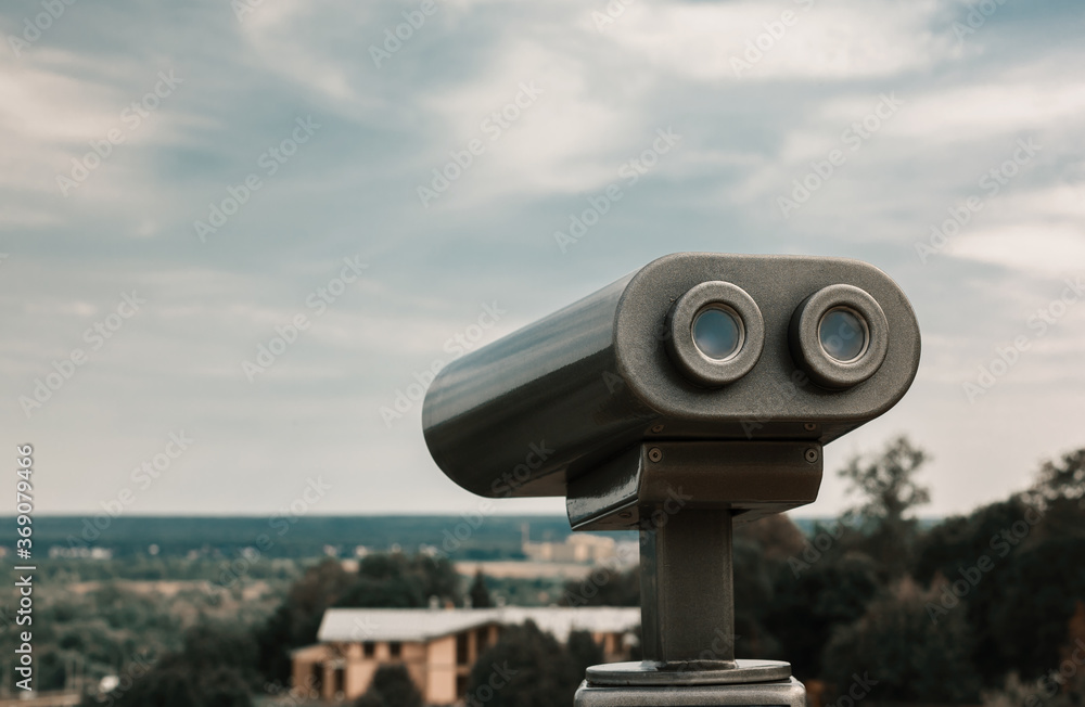 Touristic telescope overlooking city park. Metallic observation binoculars closeup with left copy space. Toned