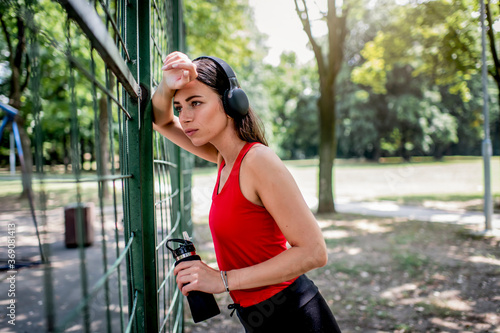 Young Caucasian athlete woman resting after outdoor run, leaning on fence.