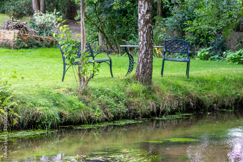 Garden chairs and garden table directly at a little creek and floating river, birch trees and idyllic scene are the perfect travel destination and hiking-tour or canoe trip recreation point