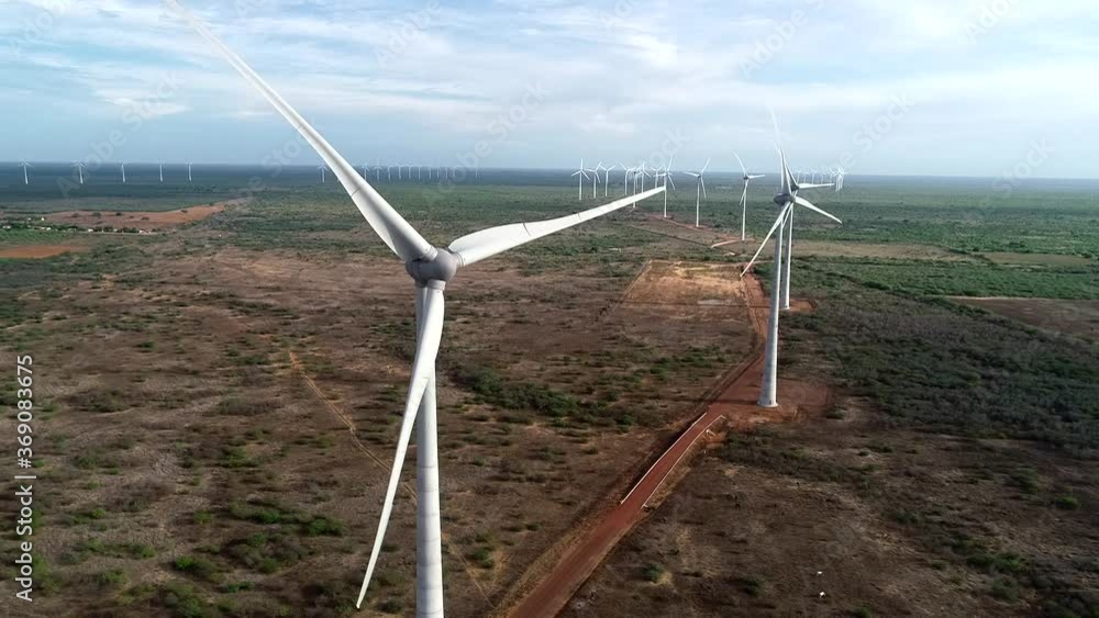 Drone filming a beautiful wind farm approaching a machine and then lateral movement towards the other wind turbines, soft light Drone filming a beautiful wind farm approaching a machine and then lateral movement towards the other wind turbines, soft light