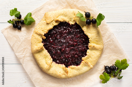 Open pie from shortcrust pastry with black currant, delicious jostaberry galette on white background © pundapanda