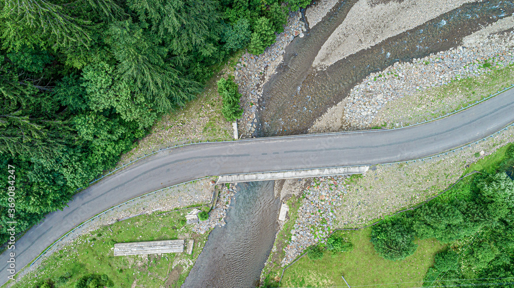 Automobile bridge over the river on the background of the forest in the mountains. Photo from the drone.