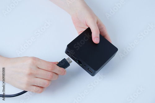 Hands of caucasian woman connects hdmi cable TV box black box. White background.