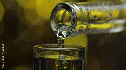 Barman pour frozen vodka from bottle into shot glass against shiny gold party celebration background