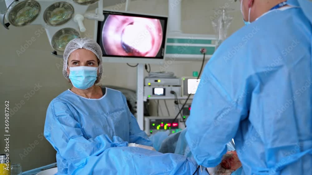 Team of doctors during surgery. Monitor shows patient's organs at the operating process in hospital. Health specialists in medical uniform and mask conduct an operation. Team of doctors during surgery. Monitor shows patient's organs at the operating process in hospital. Health specialists in medical uniform and mask conduct an operation.