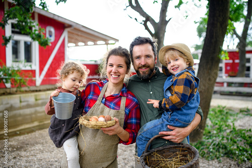 Portrait of family with small children standing on farm, holding basket with eggs.