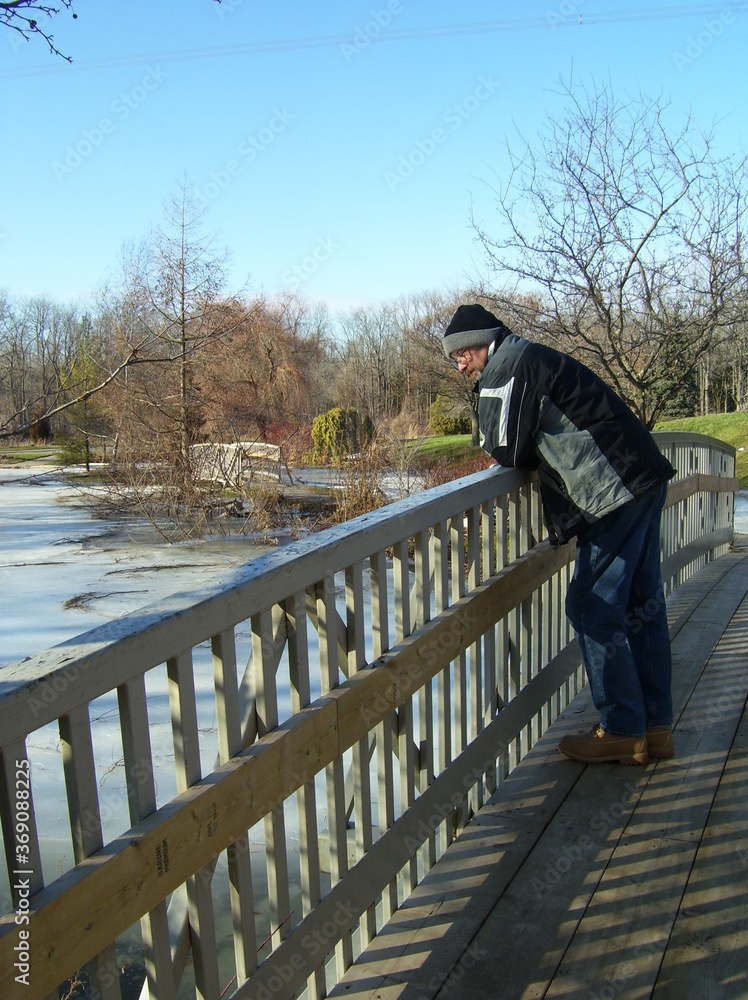 Senior man looking at the icy Spring river under a bridge in the park.