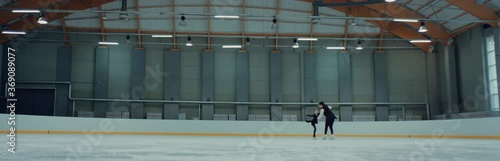 Young small girl professional figure skater parcticing with her trainer on ice. Shot on RED cinema camera with 2x Anamorphic lens, 75 FPS Slow motion photo