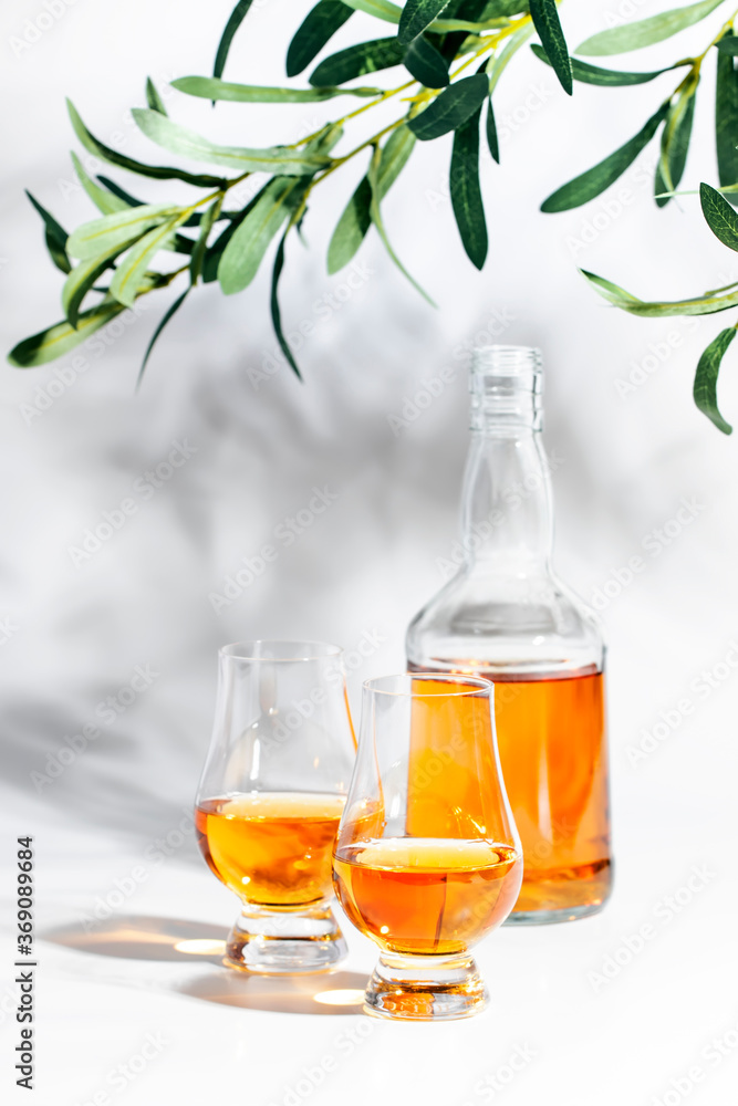 Scotch Whiskey without ice in glasses and bottle, white background with hard light, shadows and sun glare, copy space