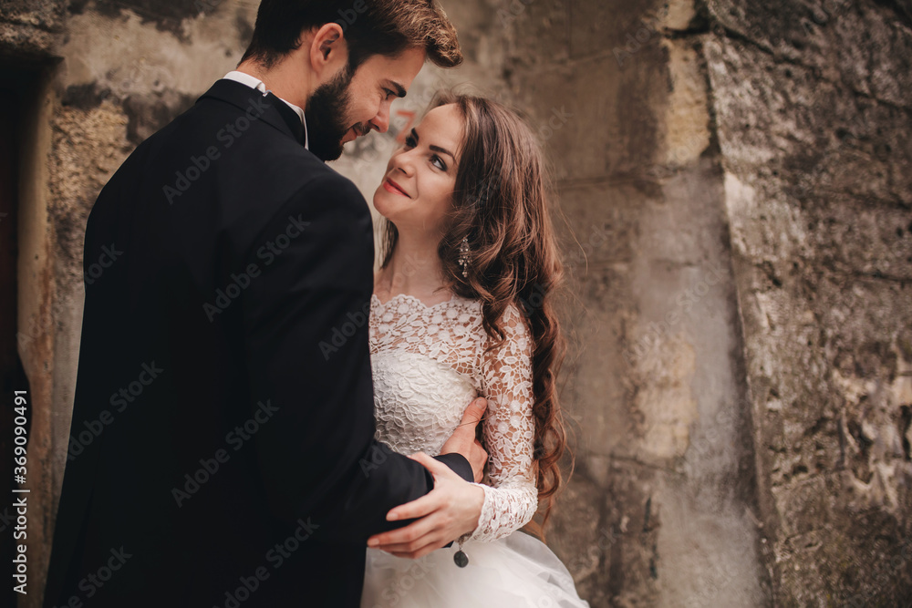 Happy newlywed couple hugging and kissing in old European town street, gorgeous bride in white wedding dress together with handsome groom. wedding day.