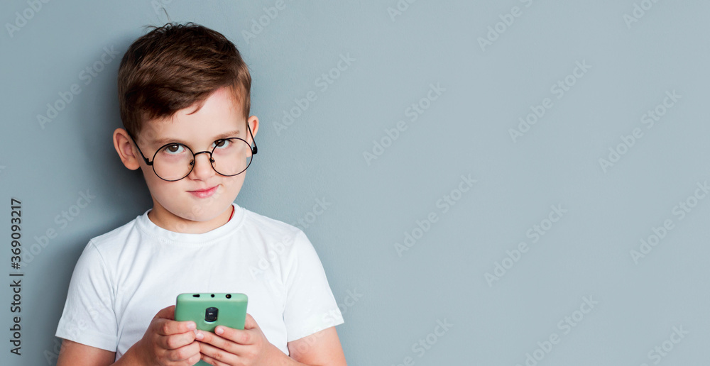 Handsome excited young boy wearing white t-shirt standing isolated over gray background, playing games on mobile phone Handsome excited young boy wearing white t-shirt standing isolated over gray background, playing games on mobile phone